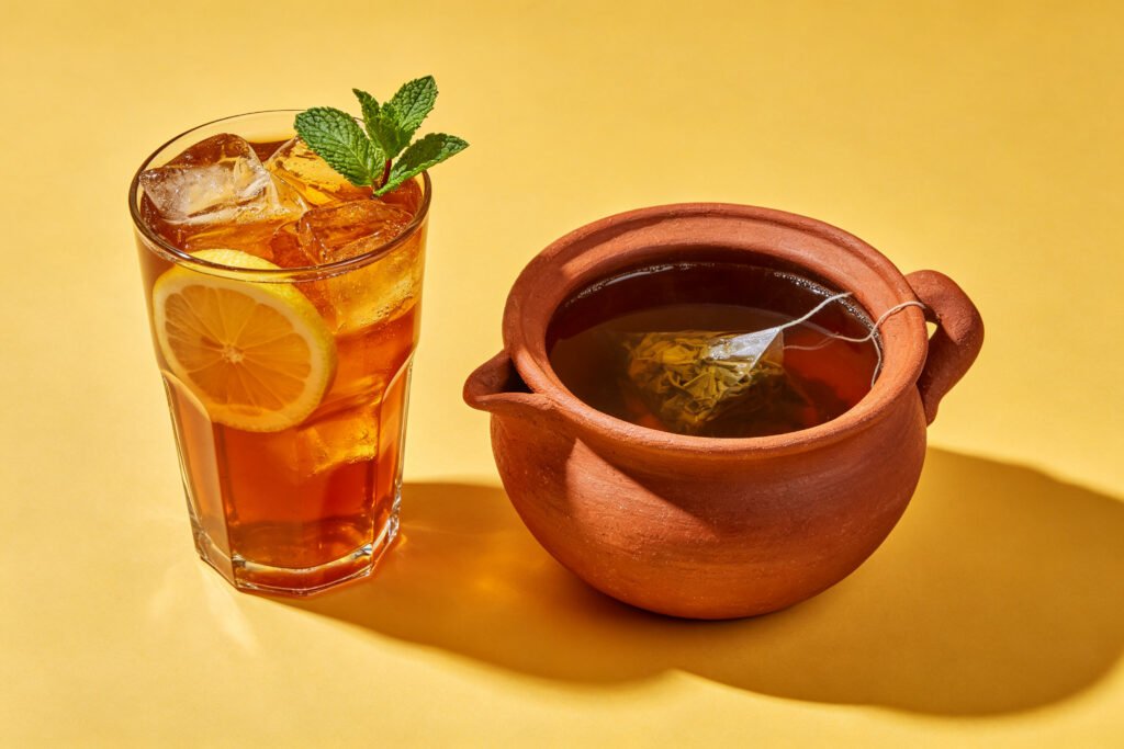 Iced lemon tea and a clay pot of brewed tea on a warm yellow background