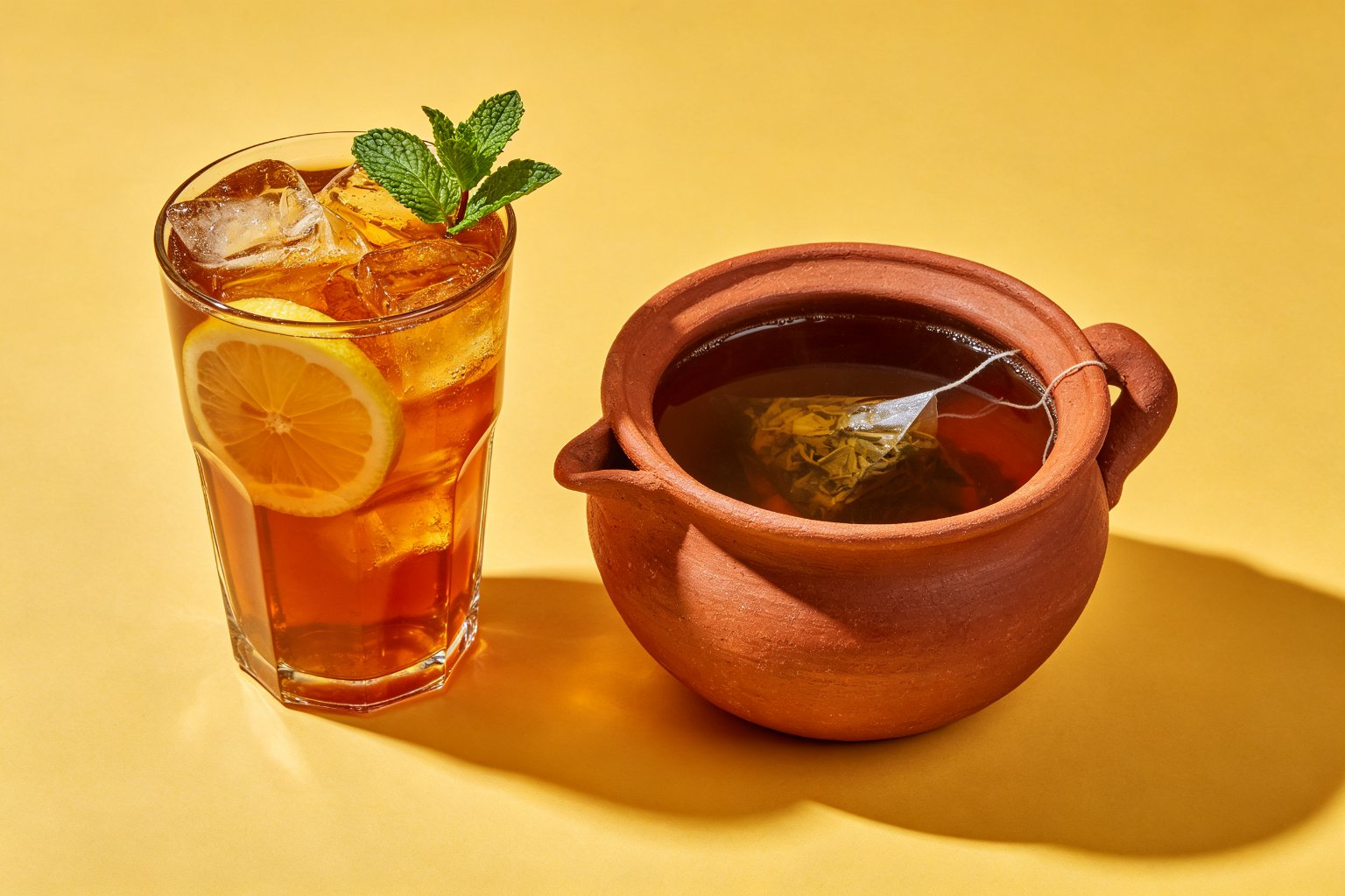 Iced lemon tea and a clay pot of brewed tea on a warm yellow background
