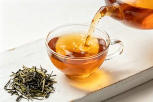 Pouring reddish Liubao tea into a glass cup with dry leaves beside it